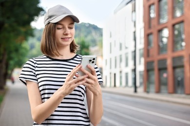 Portrait of smiling woman in baseball cap with smartphone outdoors. Space for text