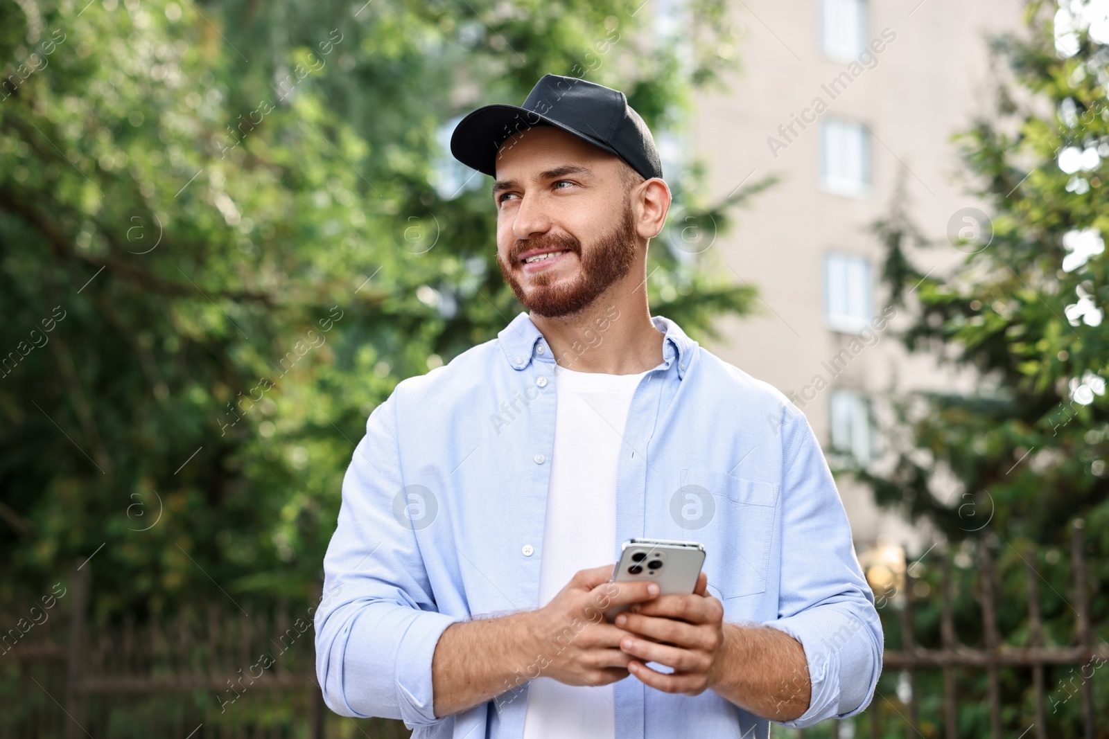 Photo of Smiling man in baseball cap with smartphone outdoors