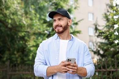 Photo of Smiling man in baseball cap with smartphone outdoors