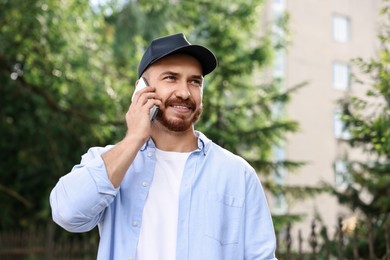 Photo of Smiling man in baseball cap talking by smartphone outdoors