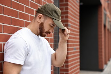 Handsome man in baseball cap near building outdoors. Space for text