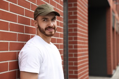 Portrait of smiling man in baseball cap near building outdoors. Space for text