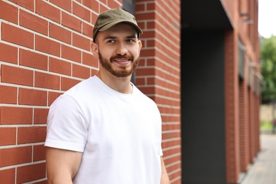 Photo of Portrait of smiling man in baseball cap near building outdoors. Space for text