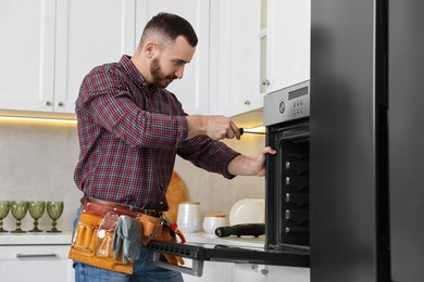 Repairman with screwdriver fixing oven in kitchen