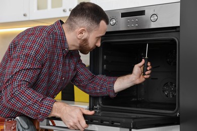 Repairman with screwdriver fixing oven in kitchen