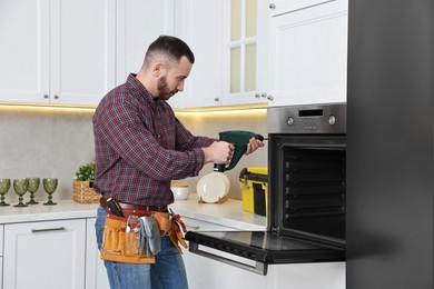 Repairman with electric screwdriver fixing oven in kitchen