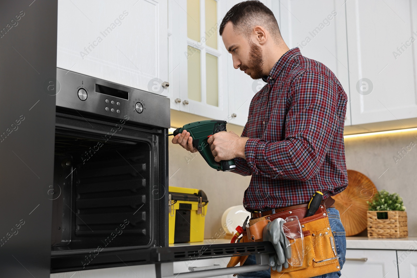 Photo of Repairman with electric screwdriver fixing oven in kitchen