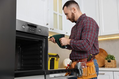 Repairman with electric screwdriver fixing oven in kitchen