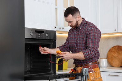 Photo of Repairman testing oven element with multimeter in kitchen