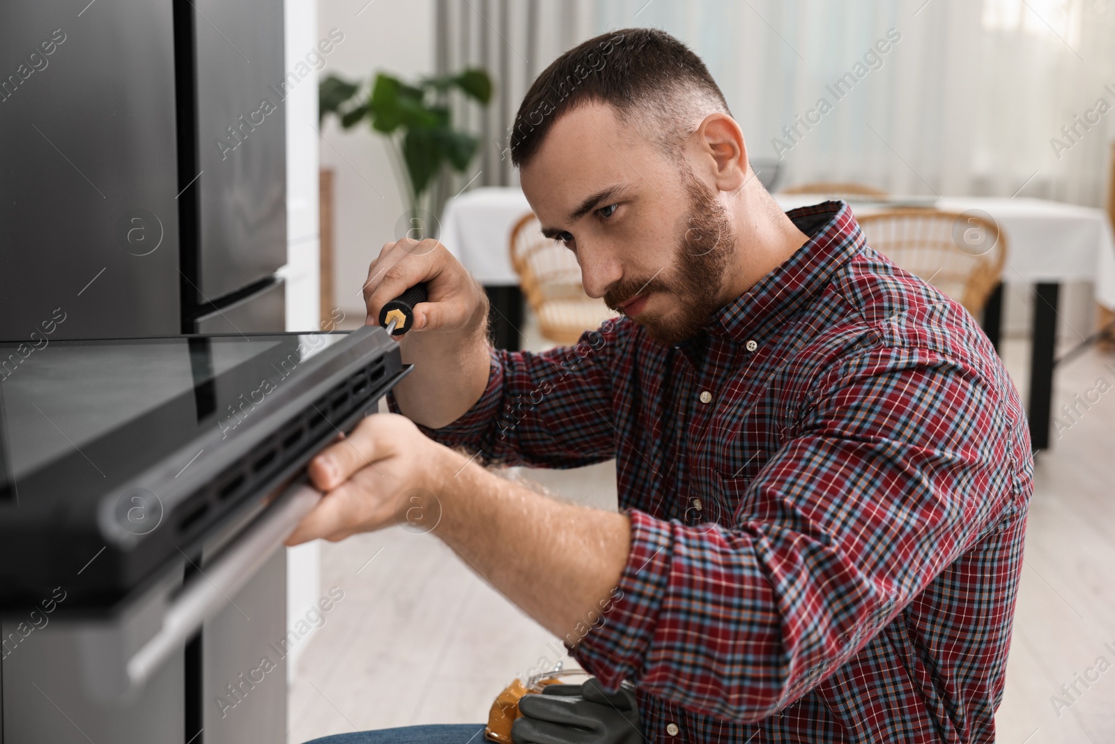 Photo of Repairman with screwdriver fixing oven at home