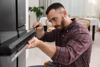 Repairman with screwdriver fixing oven at home