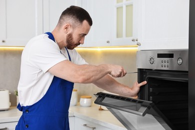 Photo of Repairman with screwdriver fixing oven in kitchen