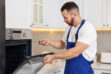 Repairman with screwdriver fixing oven in kitchen