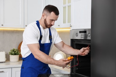 Repairman testing oven element with multimeter in kitchen