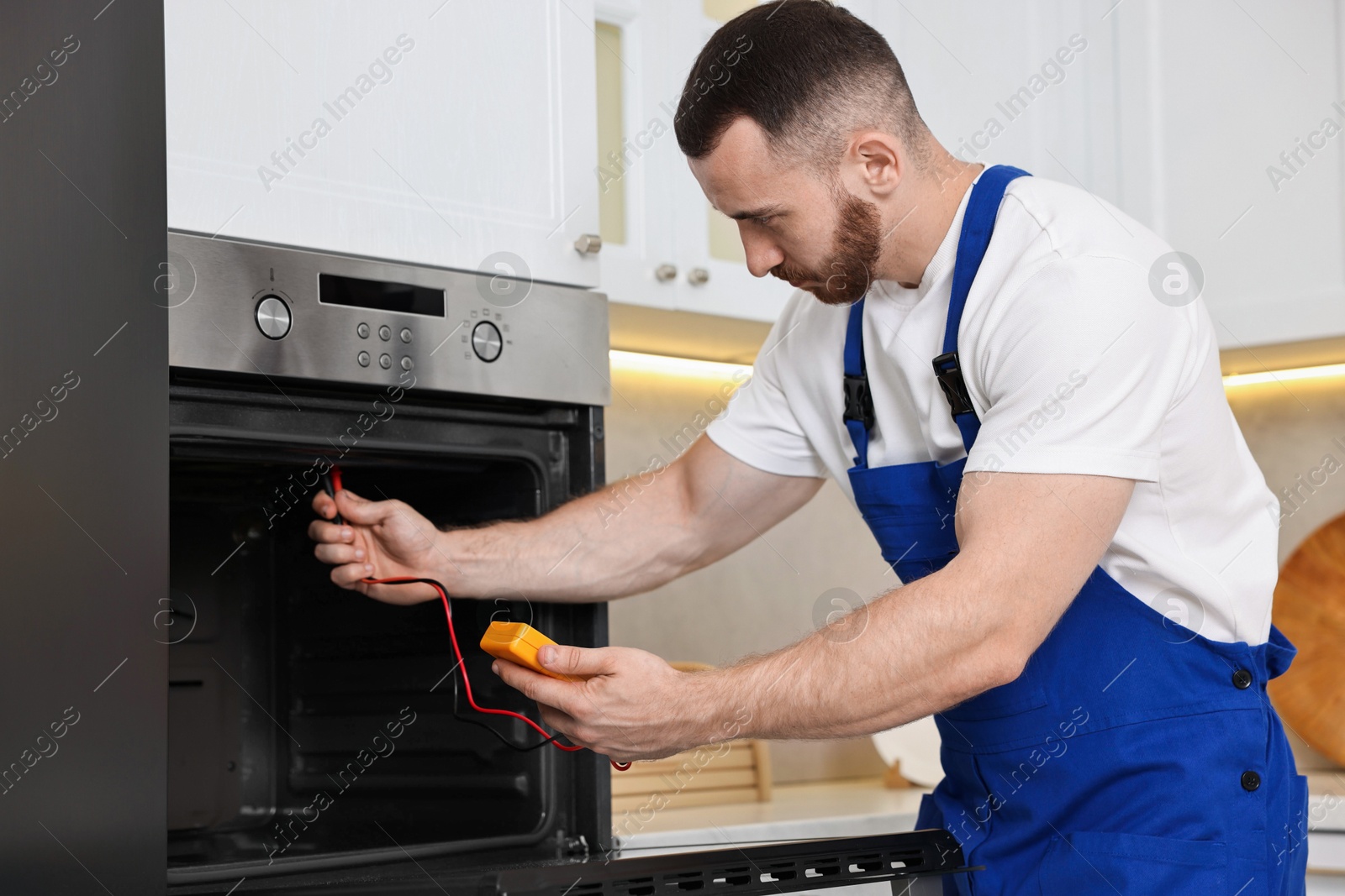 Photo of Repairman testing oven element with multimeter in kitchen