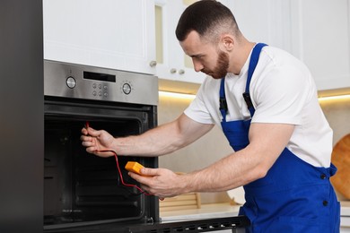 Photo of Repairman testing oven element with multimeter in kitchen