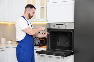 Photo of Repairman with screwdriver fixing oven at home