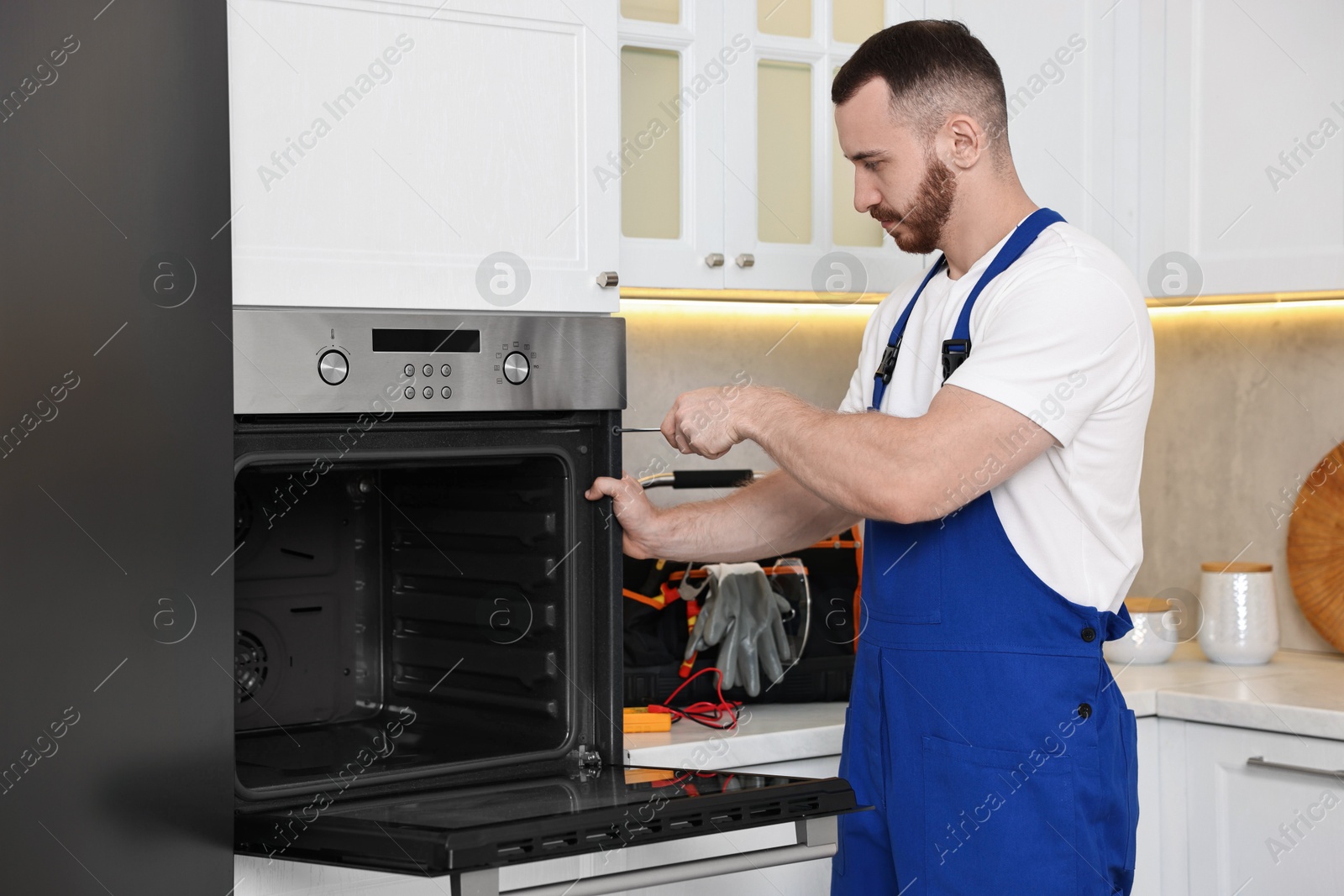 Photo of Repairman with screwdriver fixing oven at home