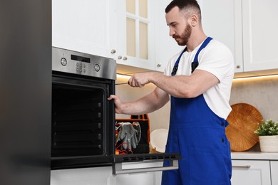 Photo of Repairman with screwdriver fixing oven at home