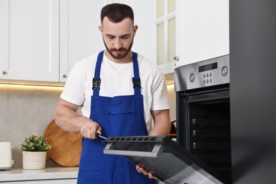 Repairman with screwdriver fixing oven at home