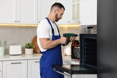 Photo of Repairman with drill fixing oven at home