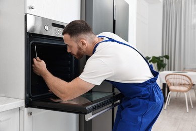 Photo of Repairman with screwdriver fixing oven at home