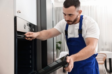 Photo of Repairman with screwdriver fixing oven at home