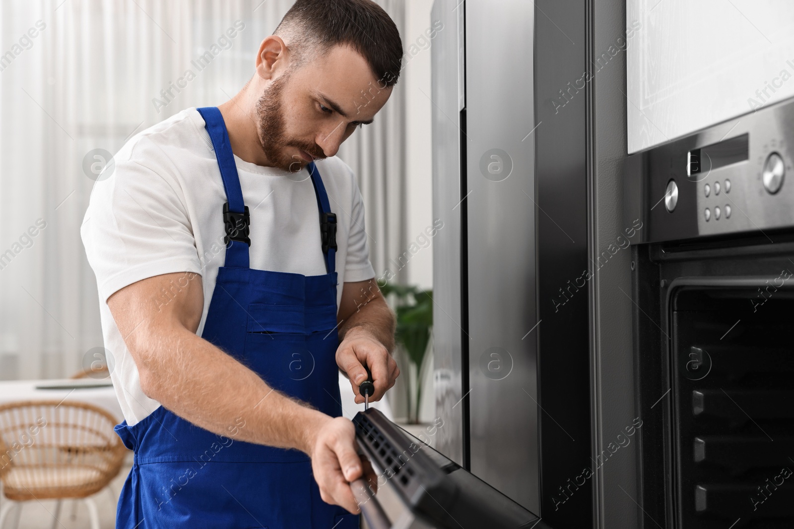 Photo of Repairman with screwdriver fixing oven at home