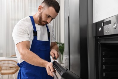 Repairman with screwdriver fixing oven at home