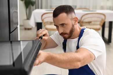 Repairman with screwdriver fixing oven at home