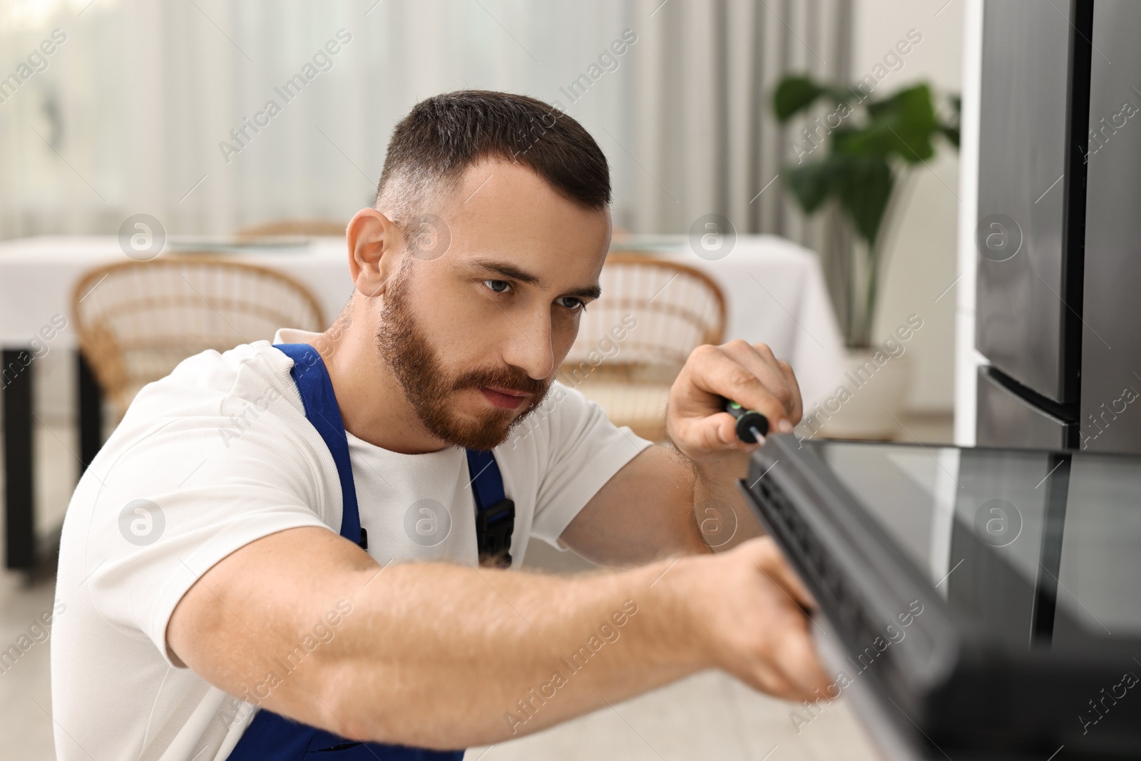 Photo of Repairman with screwdriver fixing oven at home