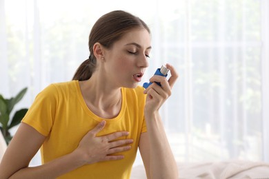 Young woman using asthma inhaler at home. Space for text