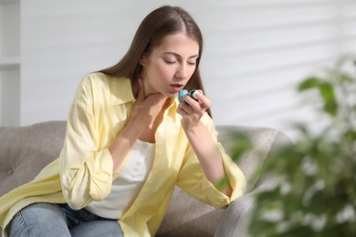 Young woman using asthma inhaler at home. Space for text