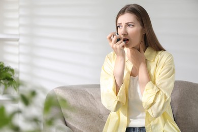 Young woman using asthma inhaler at home. Space for text