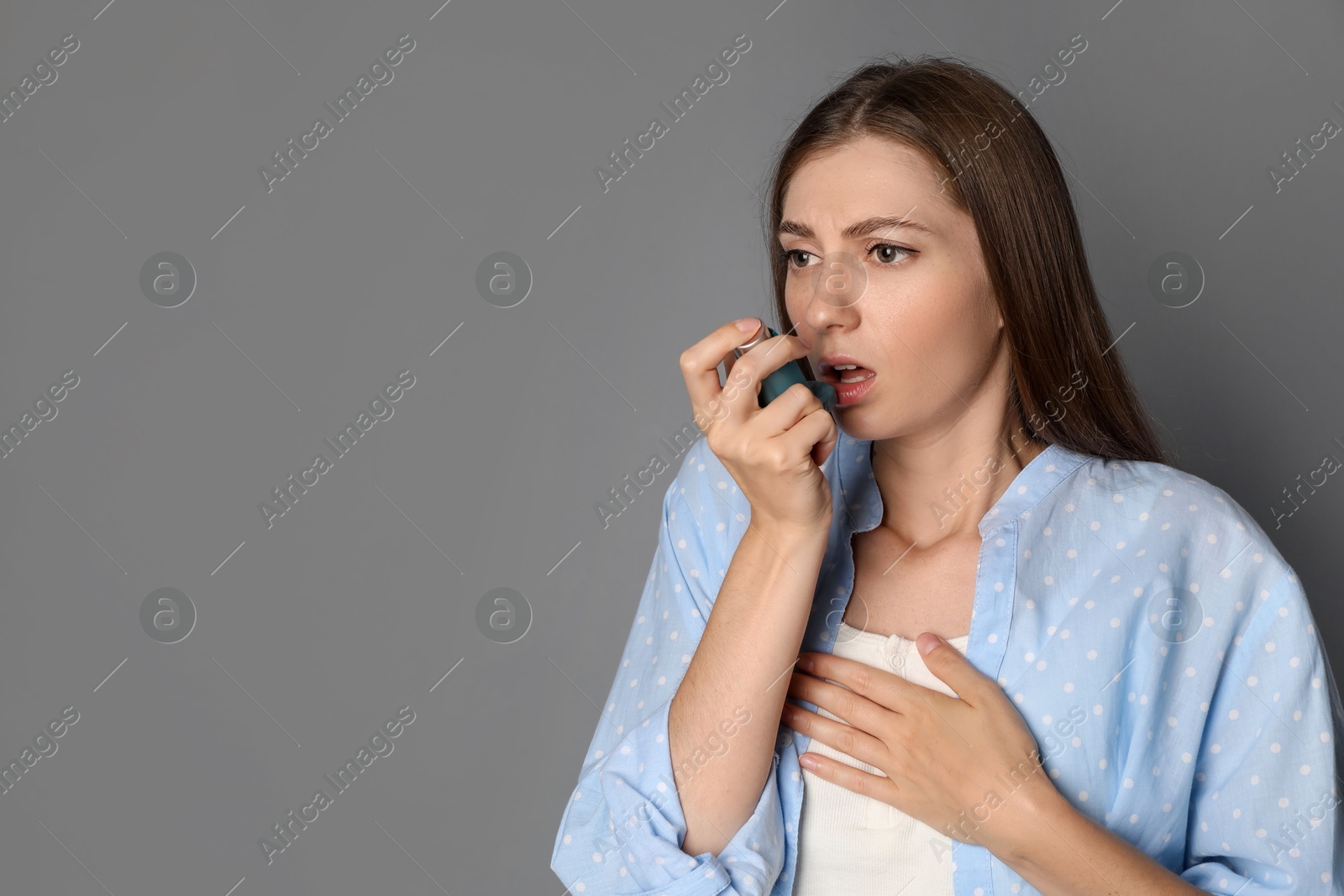 Photo of Young woman using asthma inhaler on grey background. Space for text