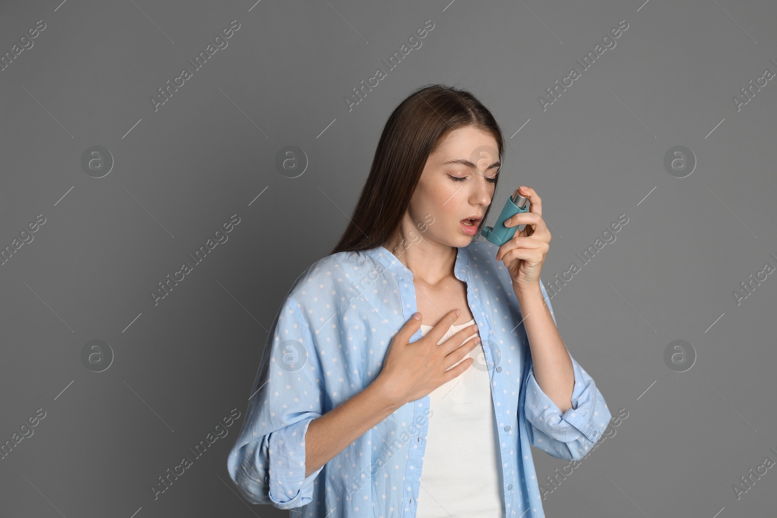 Photo of Young woman using asthma inhaler on grey background