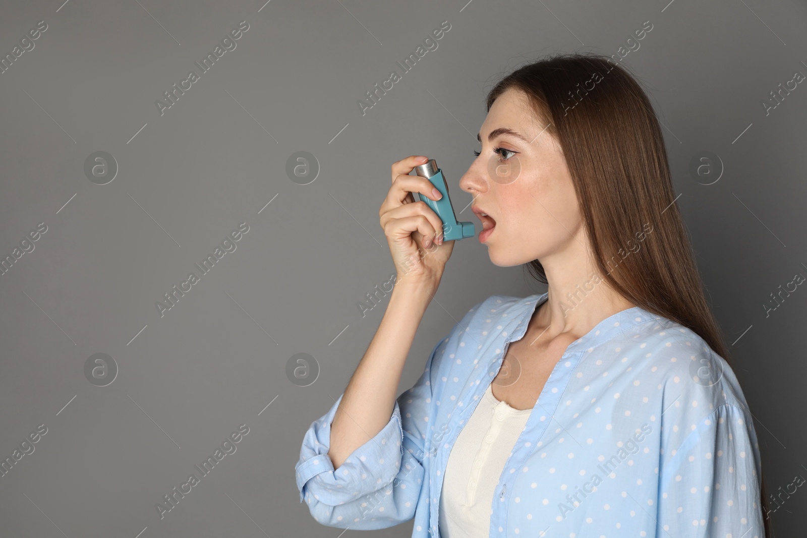 Photo of Young woman using asthma inhaler on grey background. Space for text