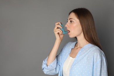 Young woman using asthma inhaler on grey background. Space for text