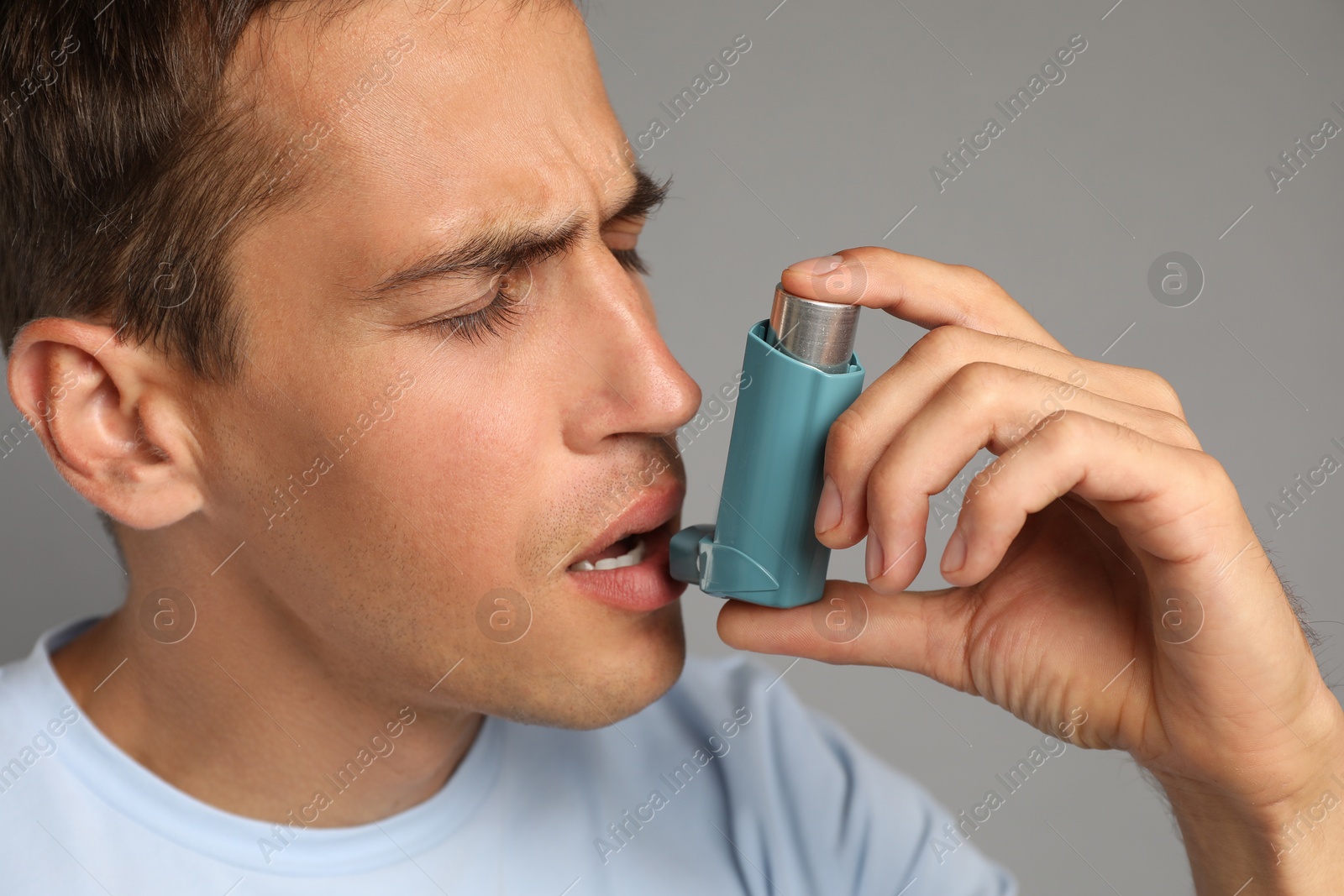 Photo of Man using asthma inhaler on grey background, closeup