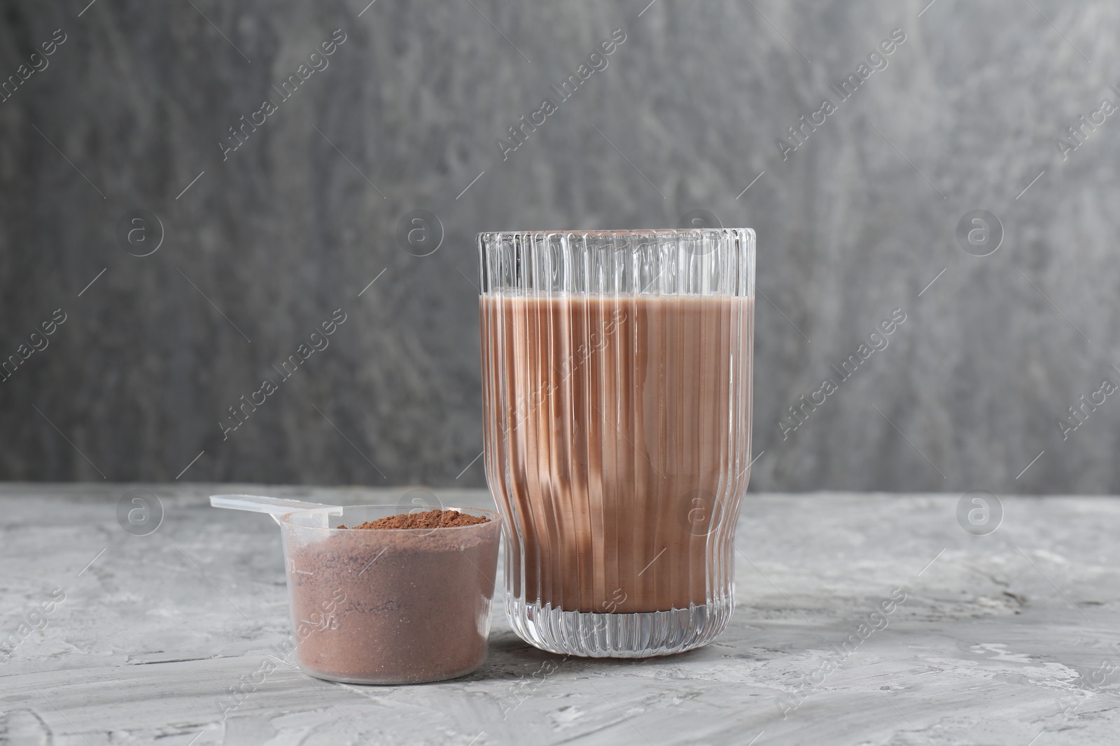 Photo of Delicious protein shake in glass and scoop with powder on grey table