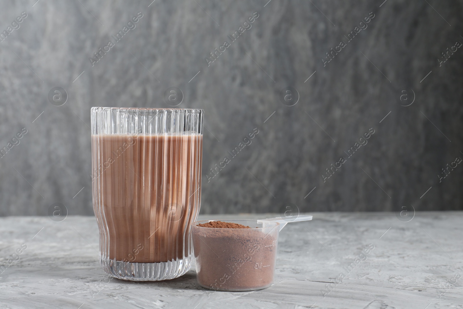 Photo of Delicious protein shake in glass and scoop with powder on grey table, space for text