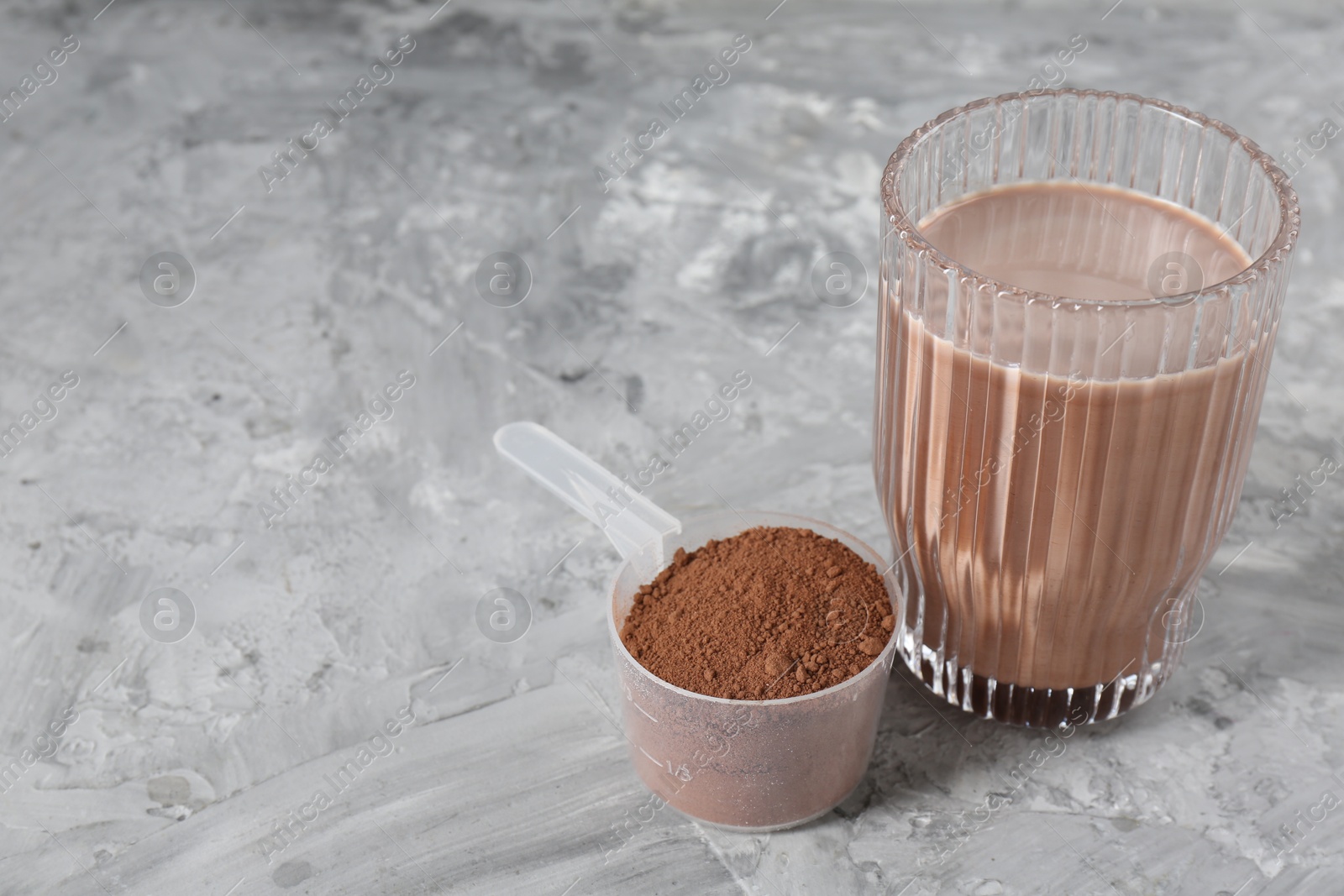 Photo of Delicious protein shake in glass and scoop with powder on grey table, closeup. Space for text