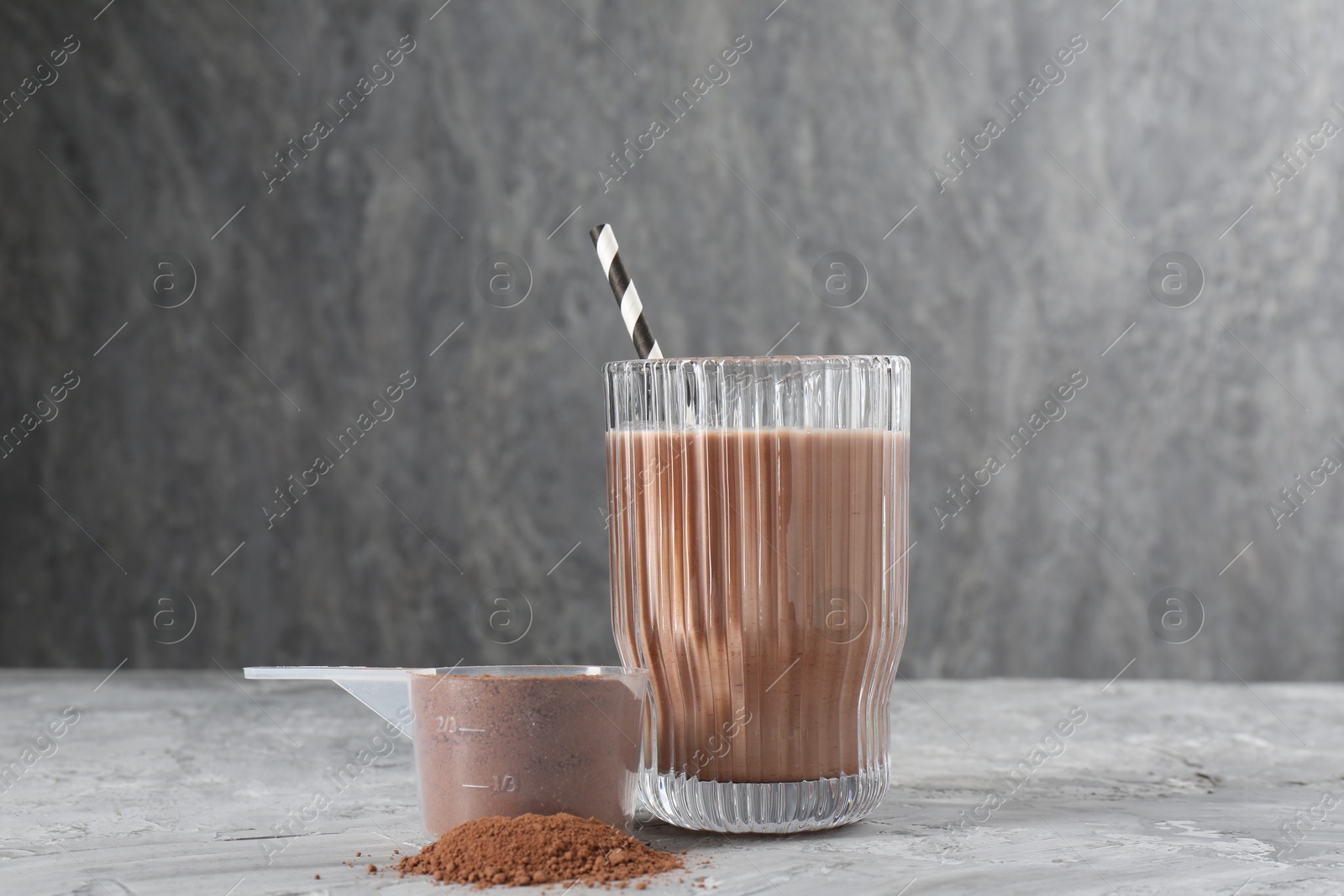 Photo of Delicious protein shake in glass and scoop with powder on grey table