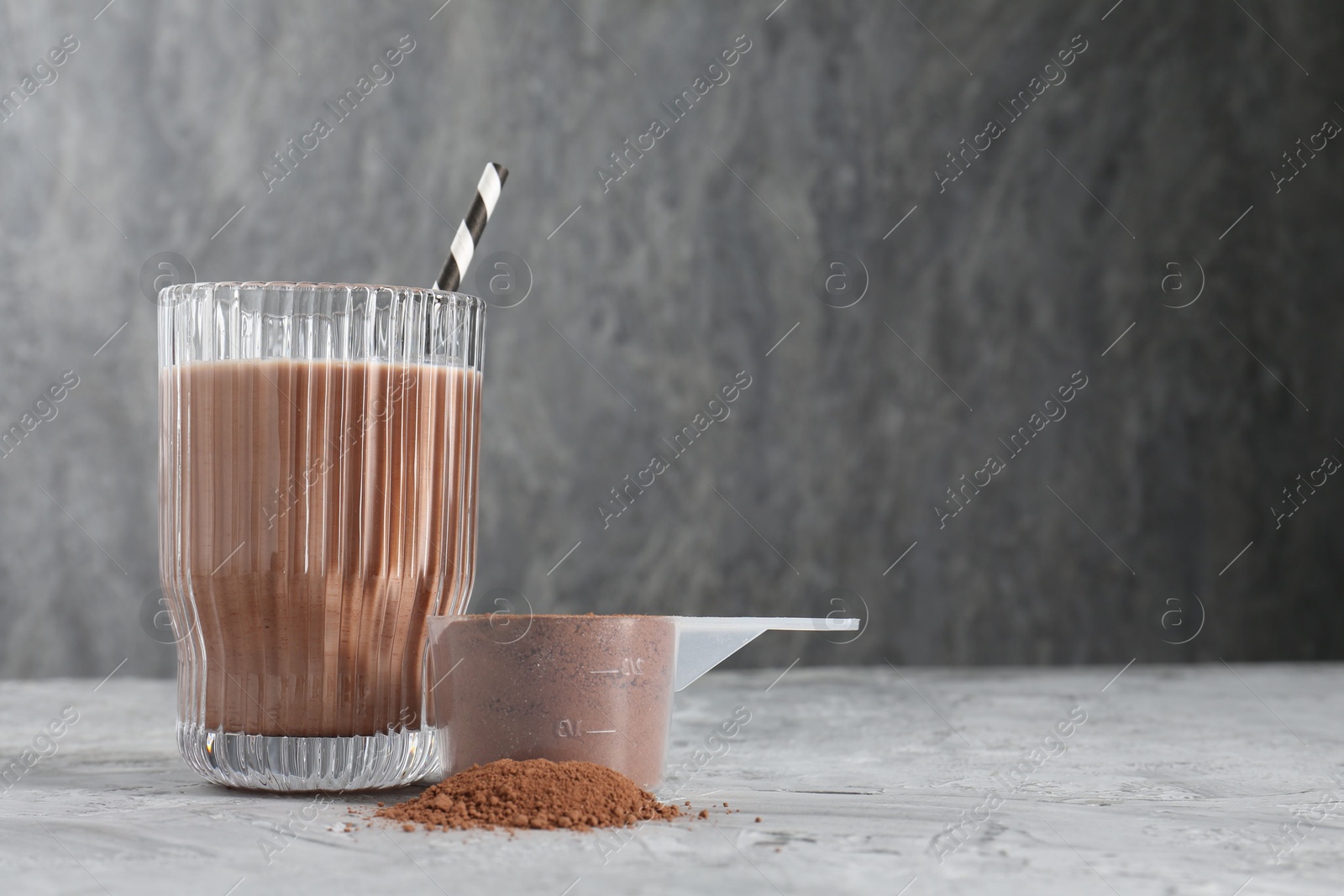 Photo of Delicious protein shake in glass and scoop with powder on grey table, space for text