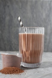 Photo of Delicious protein shake in glass and scoop with powder on grey table