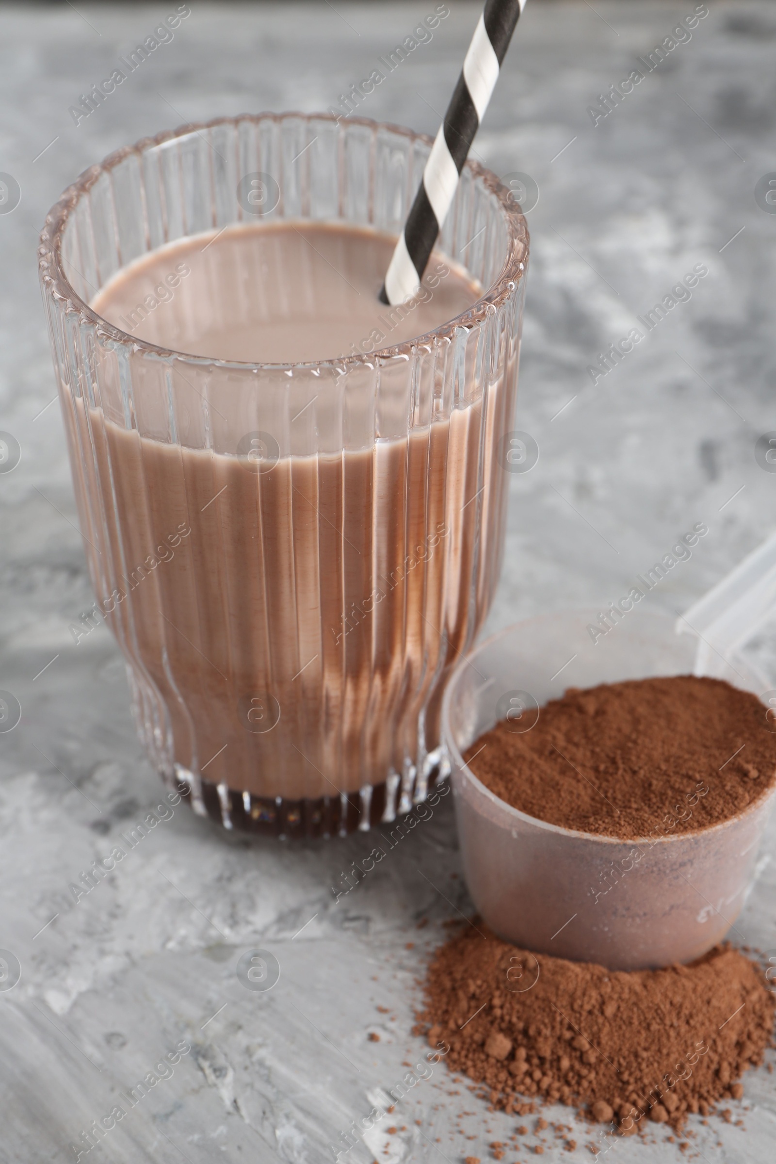 Photo of Delicious protein shake in glass and scoop with powder on grey table, closeup