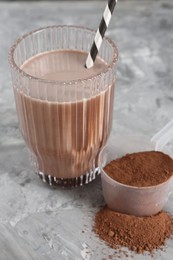 Photo of Delicious protein shake in glass and scoop with powder on grey table, closeup