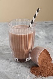 Photo of Delicious protein shake in glass and scoop with powder on grey table, closeup