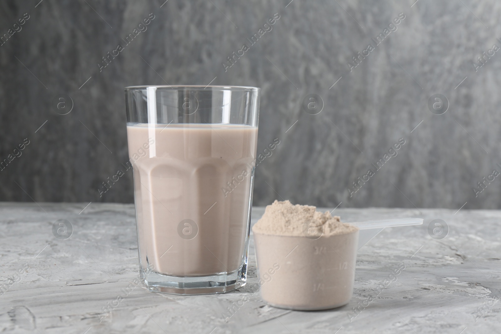 Photo of Delicious protein shake in glass and scoop with powder on grey table