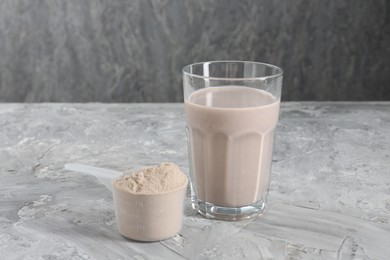 Photo of Delicious protein shake in glass and scoop with powder on grey table